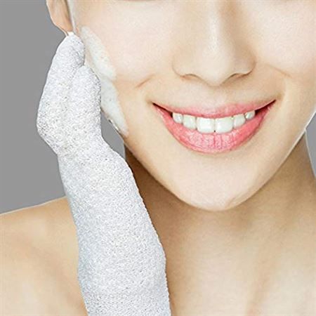 Une personne utilise un gant exfoliant blanc pour nettoyer son visage avec de la mousse.