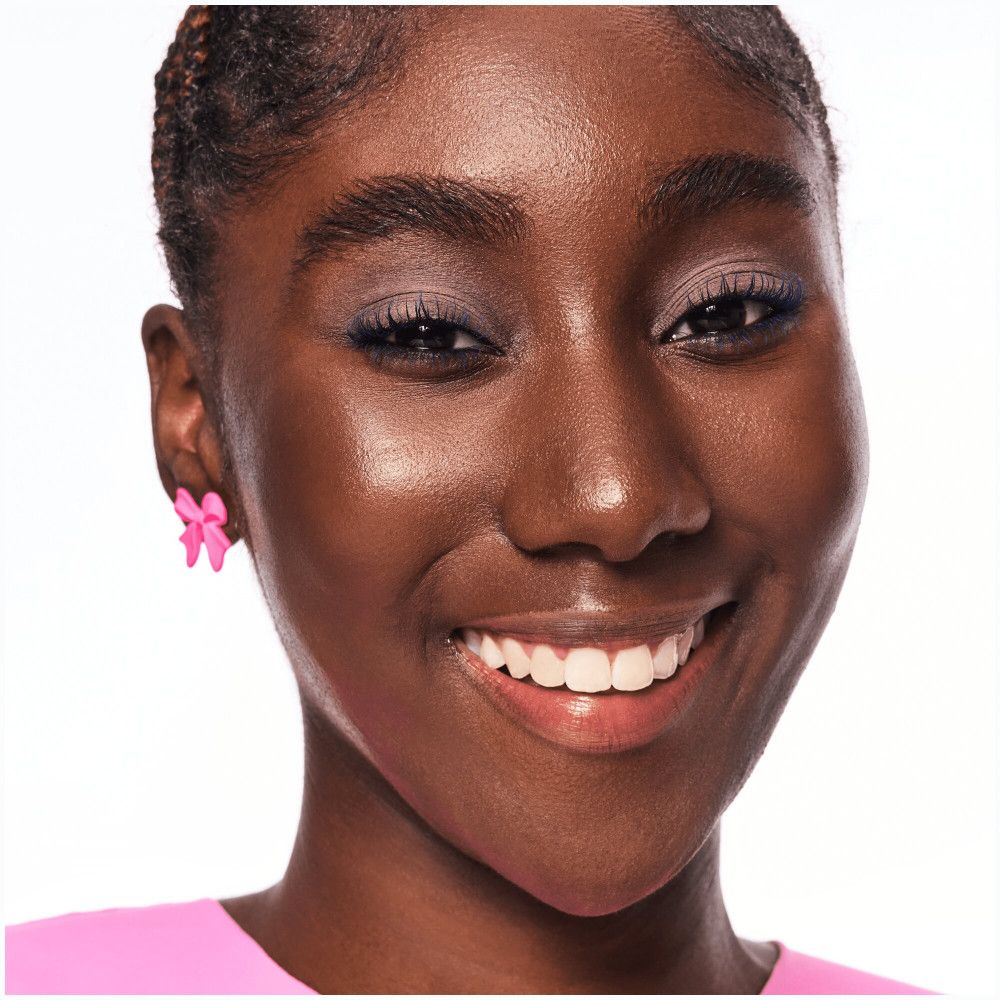 Portret van een vrouw met een donkere huid. Ze draagt roze oorbellen en lacht.