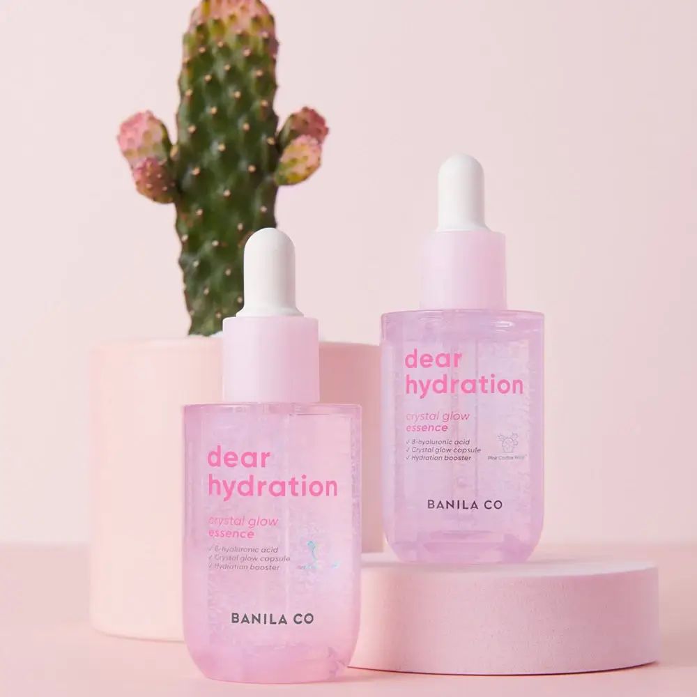 Twee flesjes BANILA CO Dear Hydration Crystal Glow Essence. Roze flesjes met witte dop, cactus op de achtergrond.