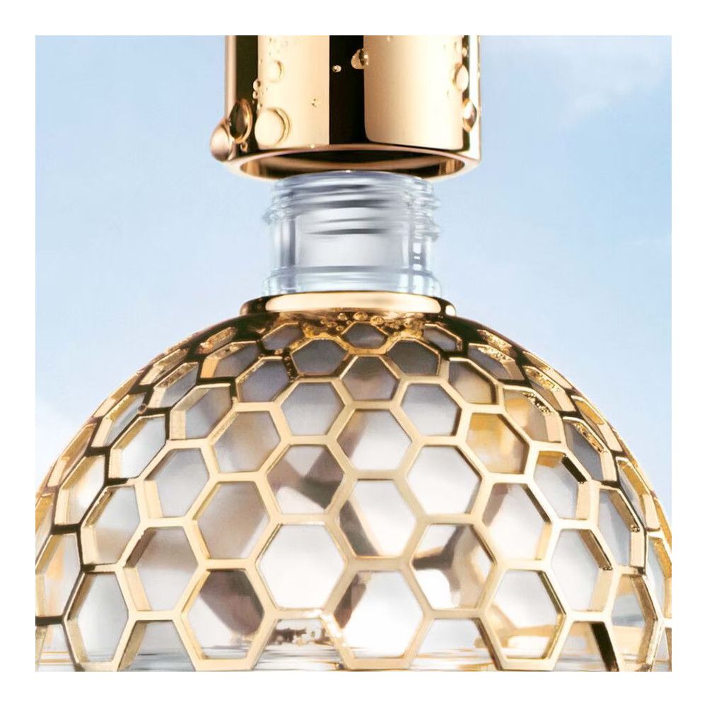 Flacon de parfum avec décor en nid d'abeille doré et bouchon doré. Vue rapprochée, fond bleu.