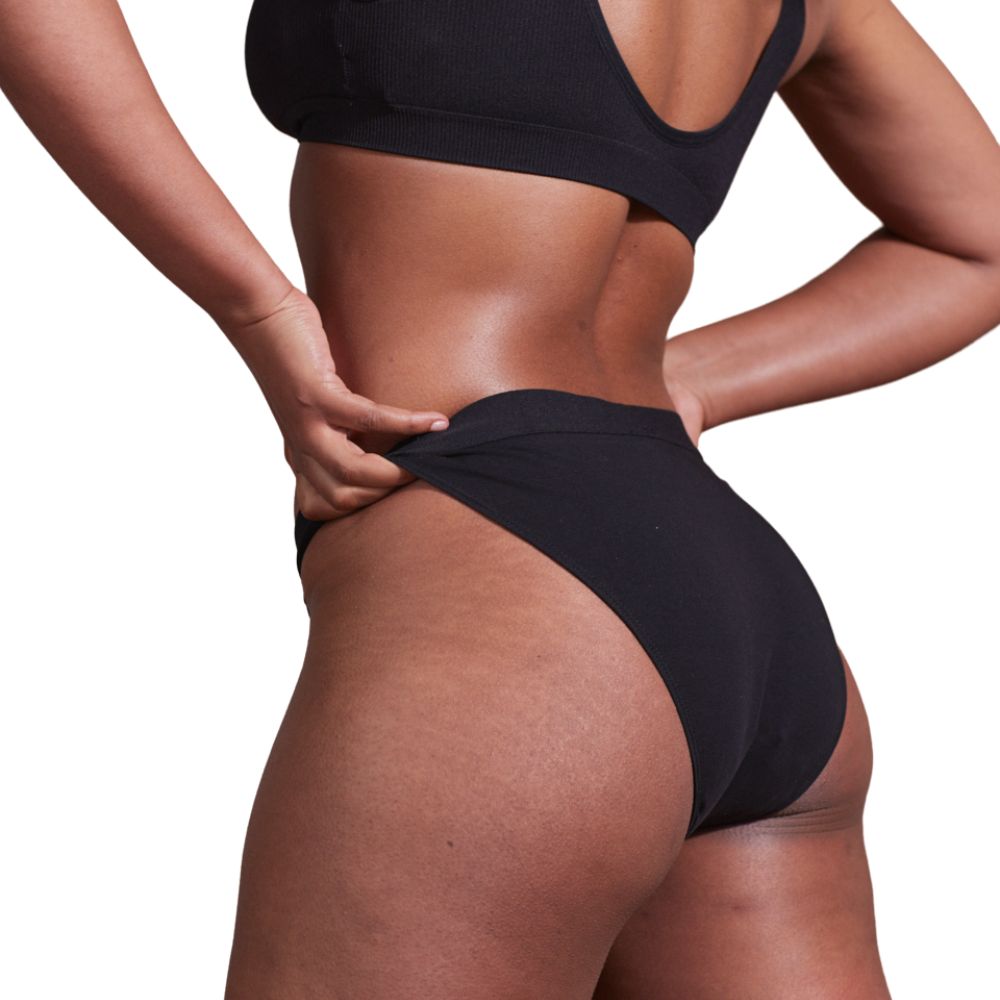 Culotte menstruelle noire en coton bio. Vue rapprochée d'une personne touchant la taille.