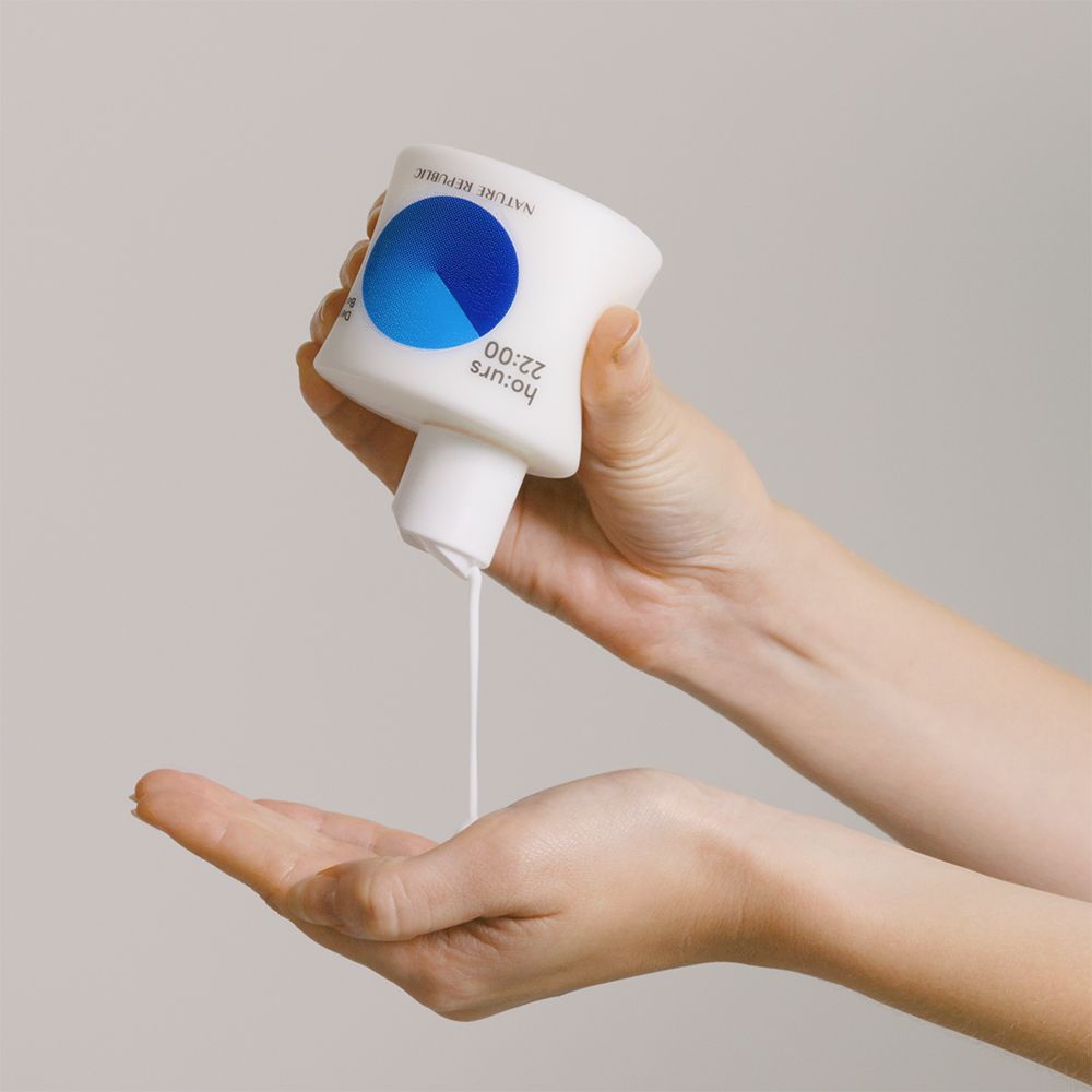 Witte fles, blauwe cirkel. Opschrift: ho:urs 22:00, NATURE REPUBLIC. Lotion wordt in de hand gegoten.