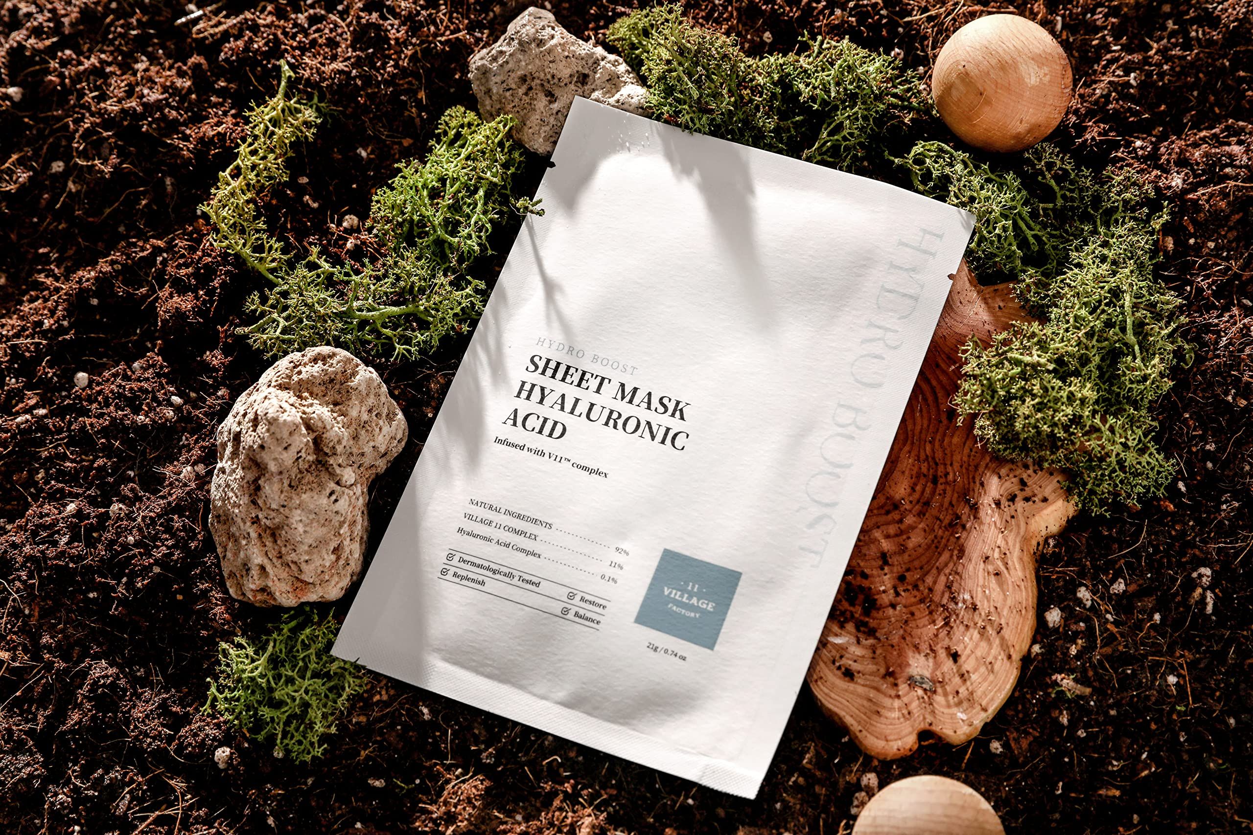 Witte sheetmasker met tekst. Geplaatst op aarde met mos en stenen. Opschrift: Sheet Mask Hyaluronic Acid.