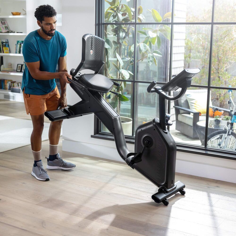 Homme ajustant un vélo d'exercice. Appareil noir avec écran. Marque : Schwinn.