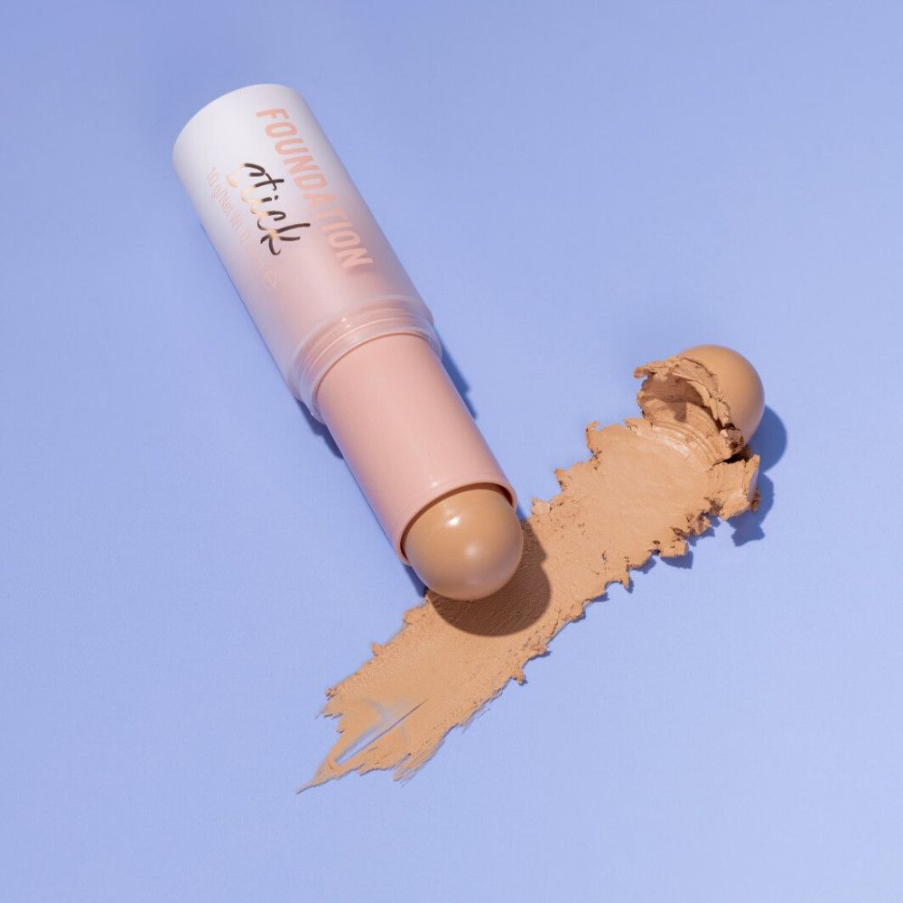 Stick de fond de teint et échantillon sur fond bleu. Le stick est rose clair et a une teinte brun clair. L'échantillon est brun clair.