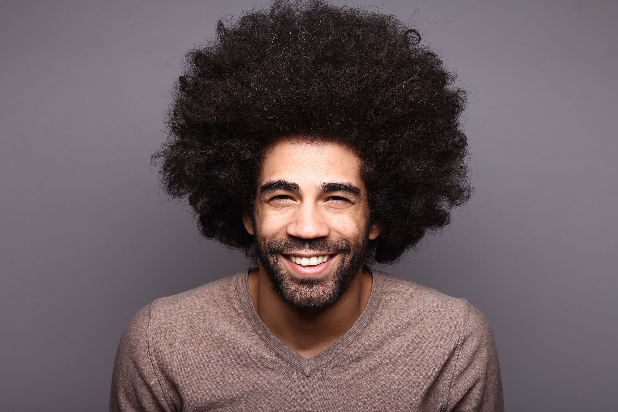 Homme aux cheveux afro volumineux souriant à la caméra.