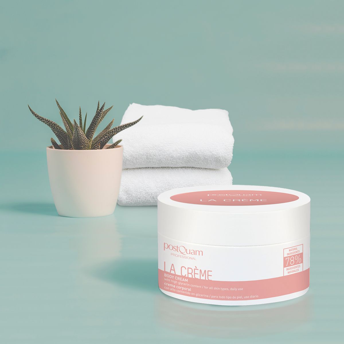 Witte pot met roze deksel, opschrift La Crème en PostQuam. Daarnaast een pot met plant en witte handdoeken.