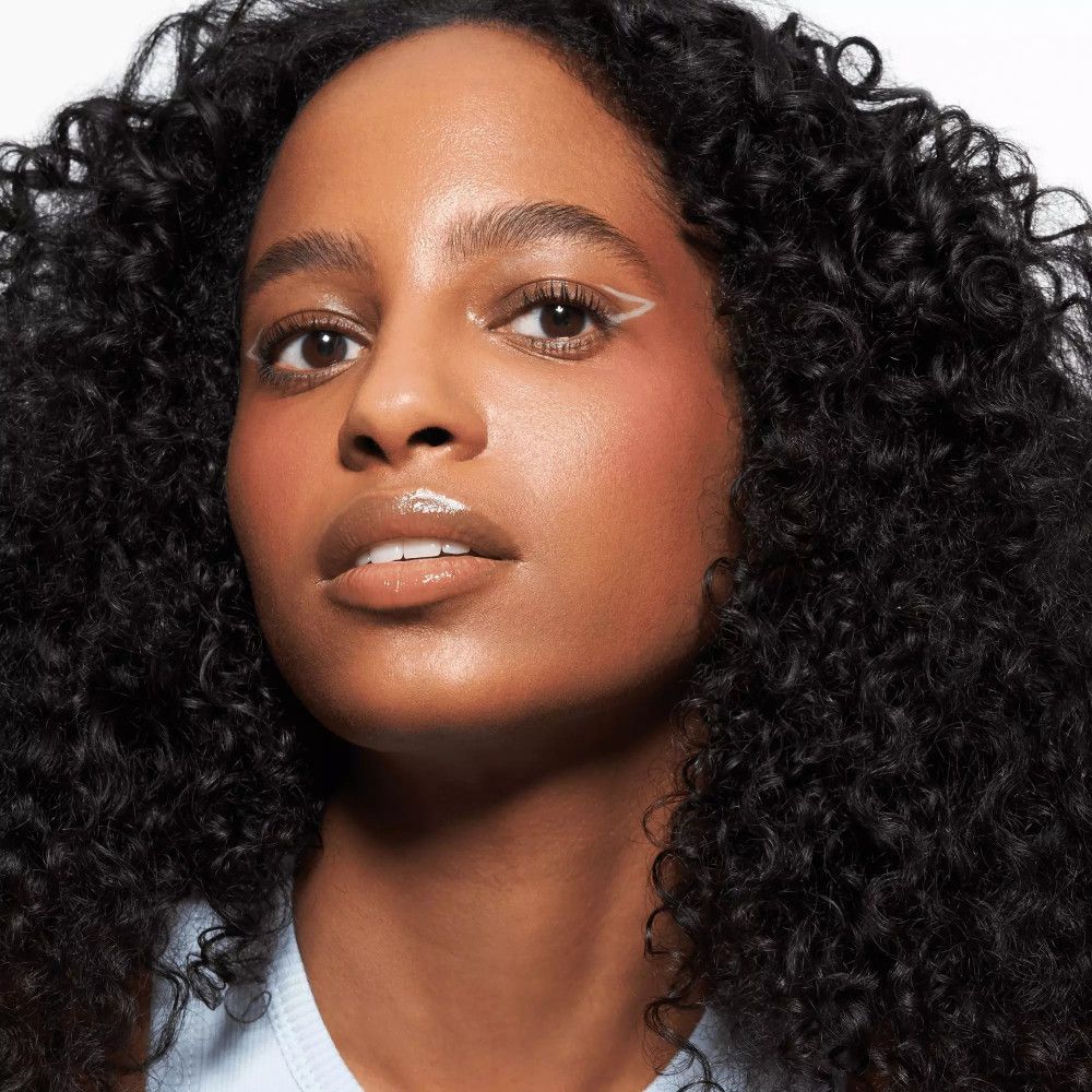 Femme aux cheveux bouclés avec trait de khôl blanc sur l'œil.