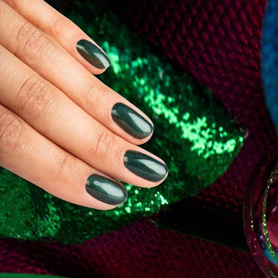 Main avec ongles vernis Silver Pine. Vernis vert sur les ongles. Fond avec paillettes vertes et décorations de Noël.