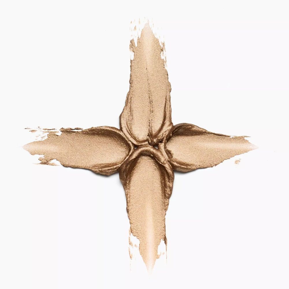 Échantillon de fard à paupières crème doré en forme de croix sur fond blanc. Texture et couleur du produit clairement visibles.