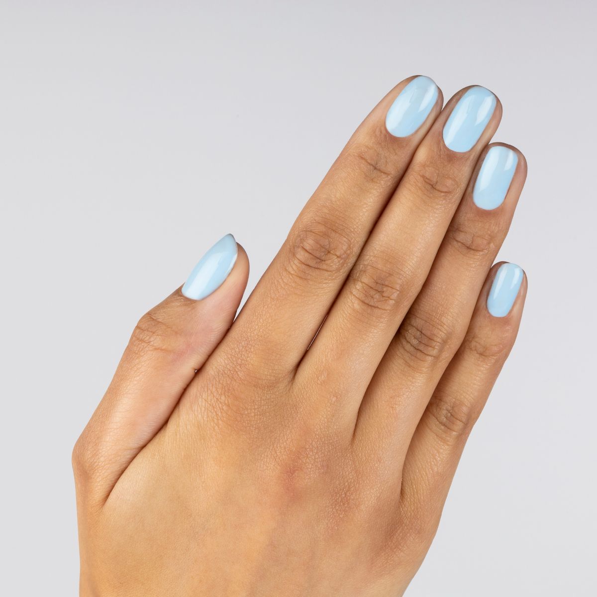 Main avec ongles peints en bleu clair. Les ongles sont peints dans une teinte bleu clair. Fond de couleur chair.