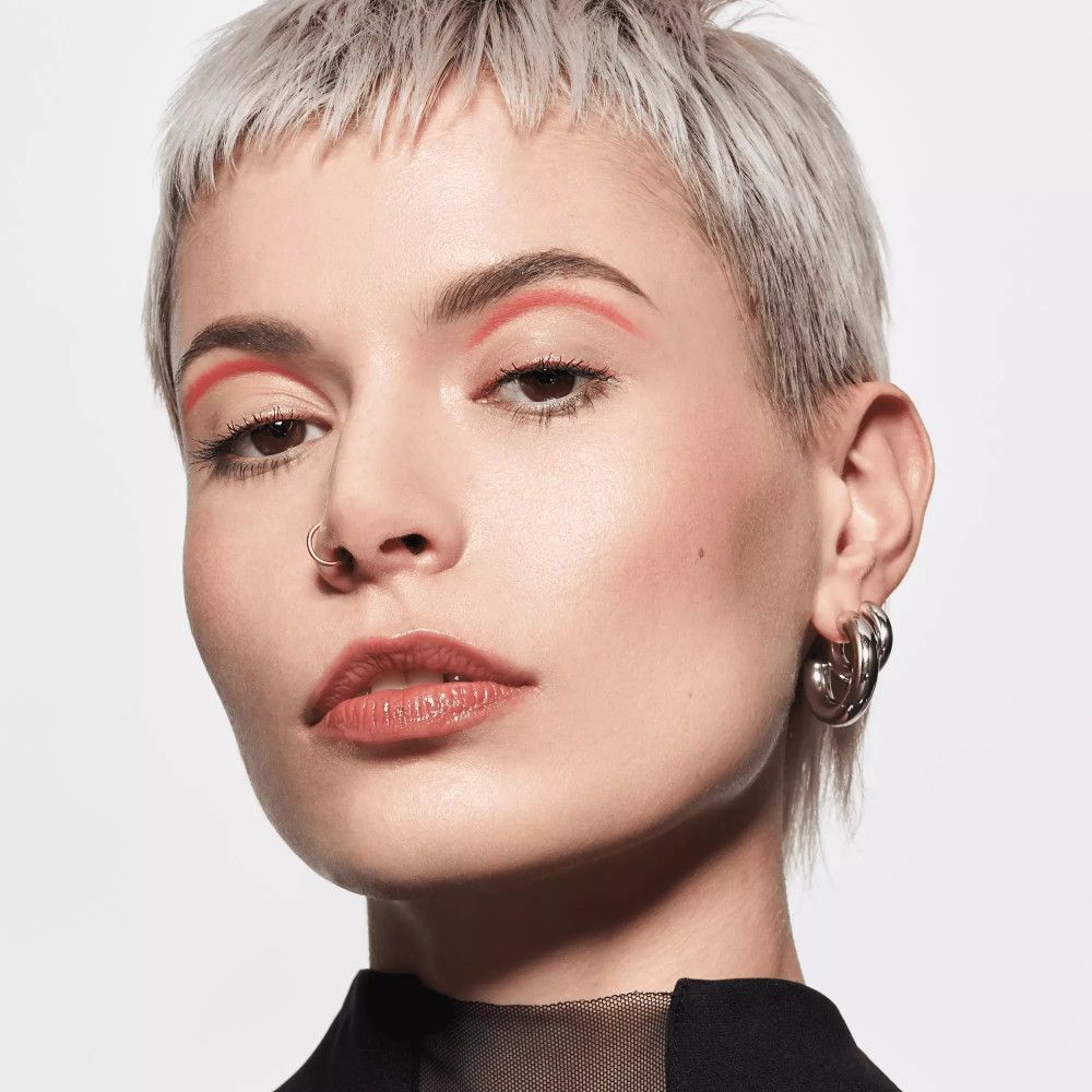 Femme aux cheveux courts, portant du baume à lèvres. Teint clair, rouge à lèvres.