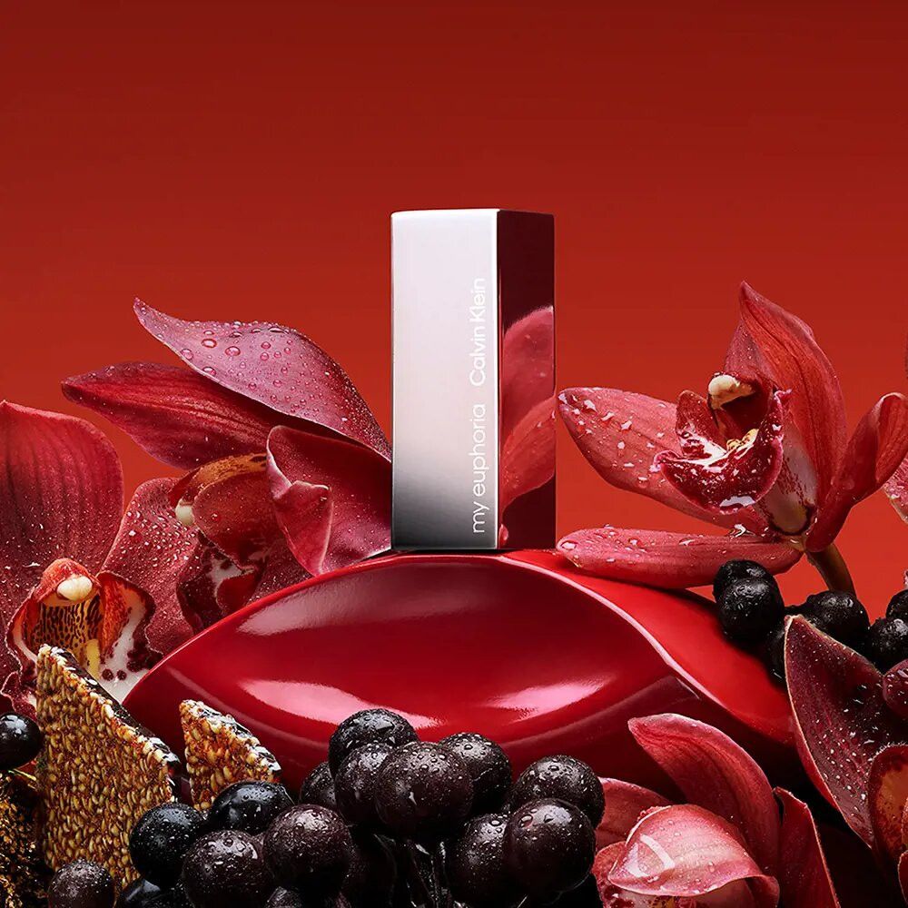 Flacon rouge avec bouchon argenté. Inscription: my euphoria Calvin Klein. Entouré de fleurs rouges.