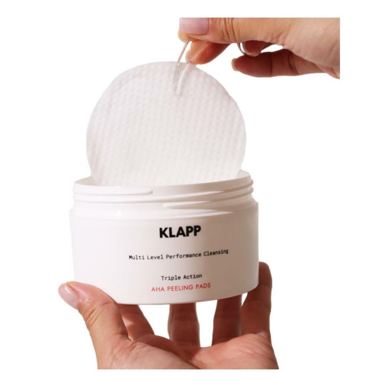Récipient blanc avec tampons. Main tenant un tampon. Inscription : Klapp, Multi Level Performance Cleansing, Triple Action, AHA PEELING PADS.