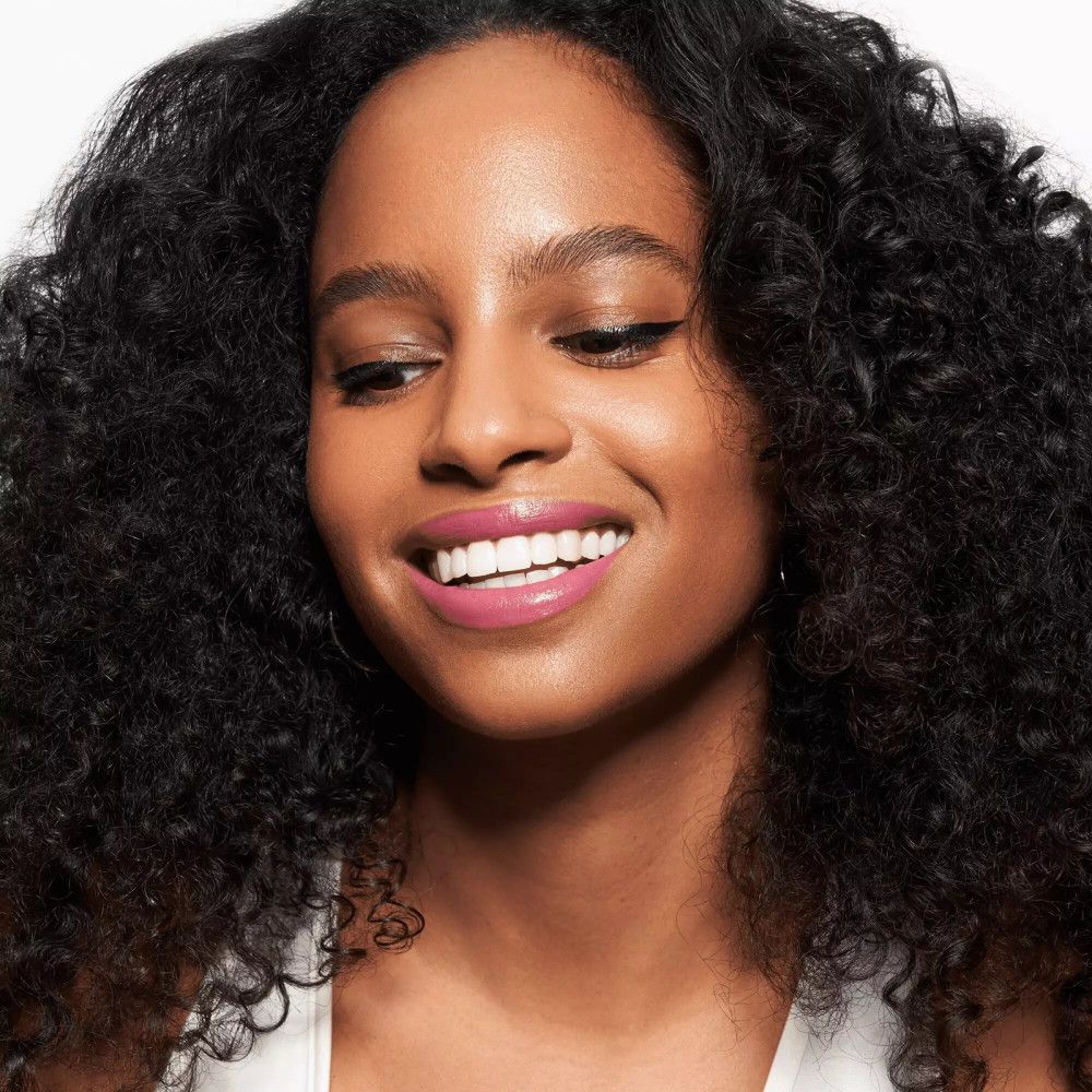 Femme aux boucles et rouge à lèvres rose. Trait d'eye-liner noir.