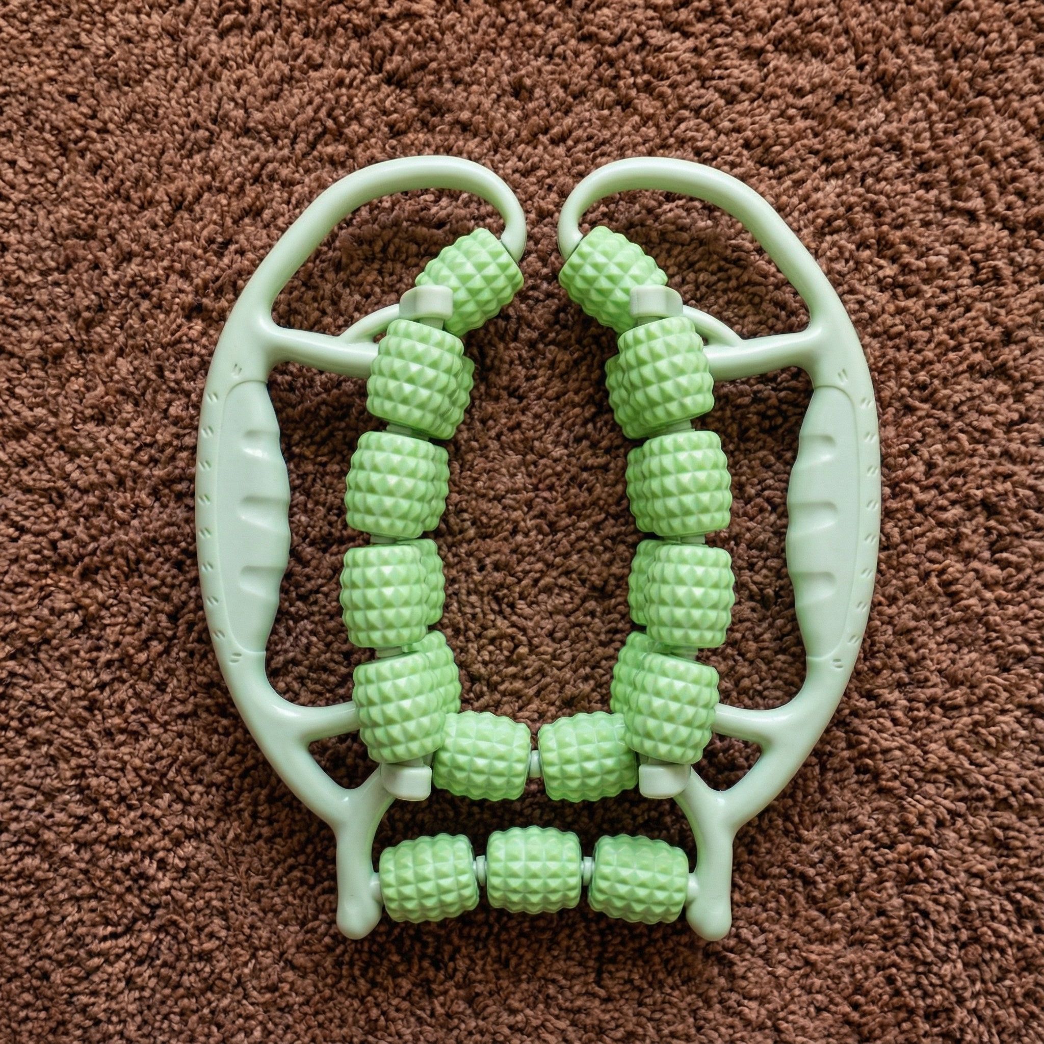 Groene massageroller met handvatten. Ligt op bruin tapijt.