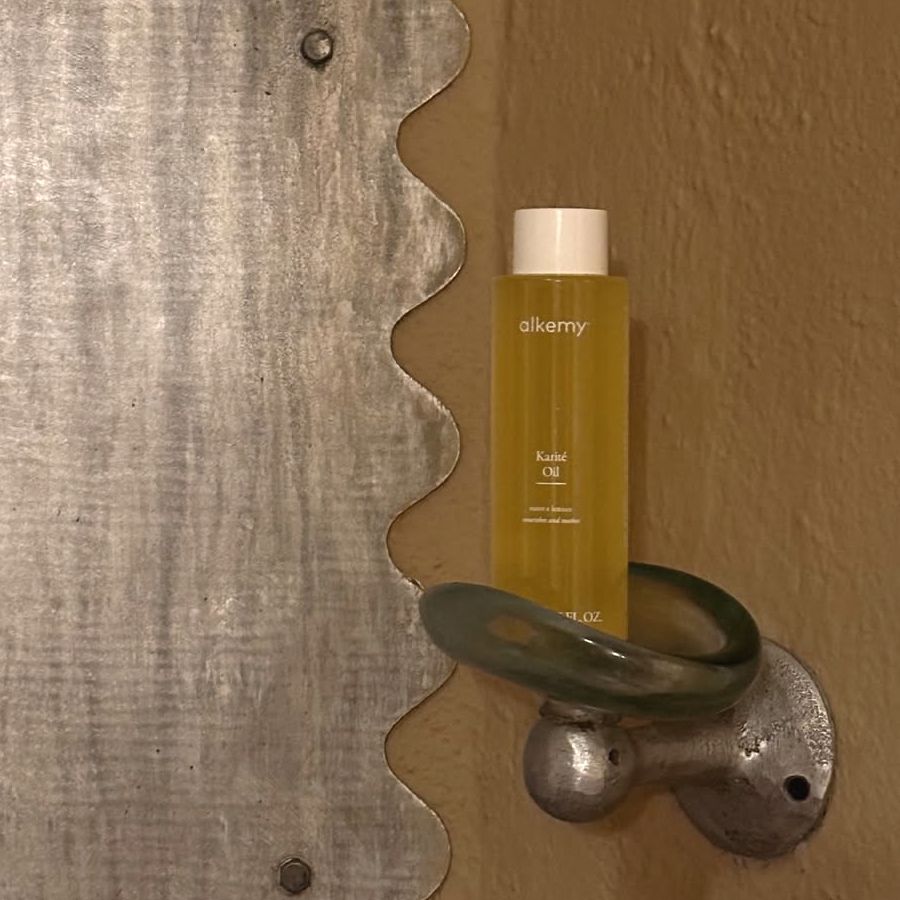 Bouteille d'huile Alkemy Karité dans un support décoratif.