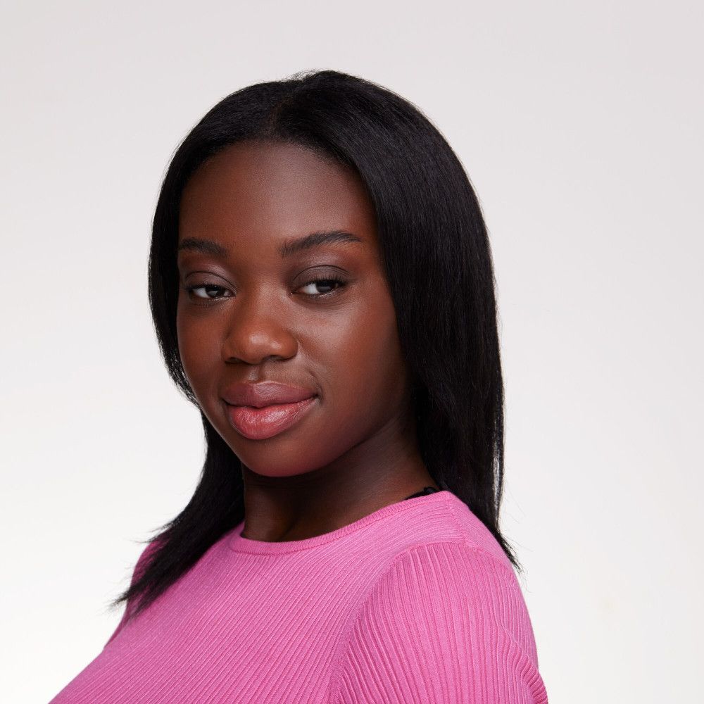 Portrait d'une femme aux cheveux noirs et un haut rose. Elle regarde de côté et sourit légèrement.