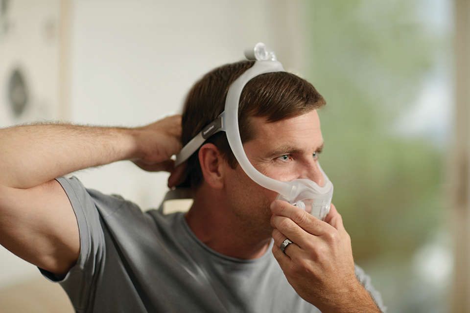 Un homme ajuste un masque nasal intégral Philips CPAP DreamWear.