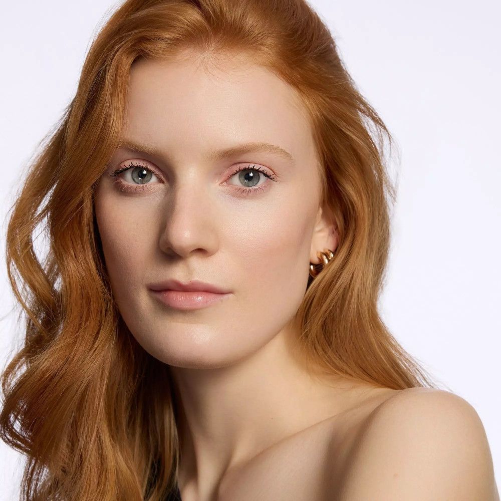 Portret van een vrouw met rood haar. Ze draagt gouden oorringen. Natuurlijke make-up.