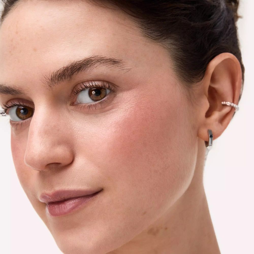 Gros plan d'un visage avec du fard à joues sur les joues. La personne porte des boucles d'oreilles.