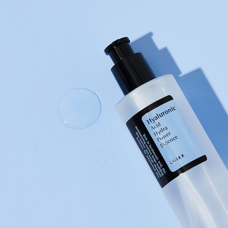 Close-up van een fles met pomp. Productnaam en merk COSRX op etiket. Op blauwe achtergrond.