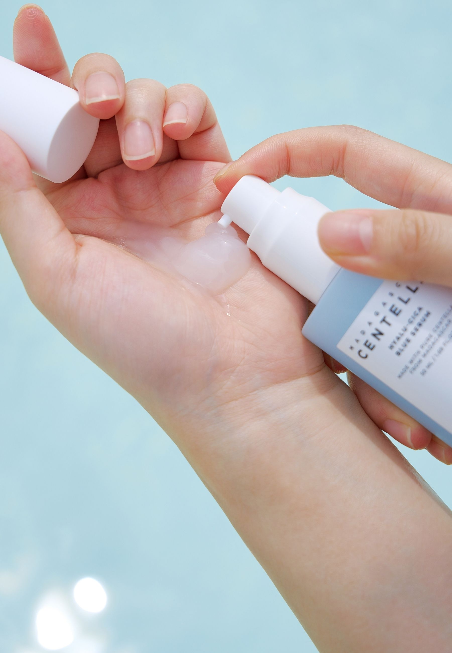 Handen houden serumfles. Opschrift: MADAGASCAR CENTELLA HYALU-CICA BLUE SERUM. Merk: SKIN1004. Serum wordt op de hand aangebracht.