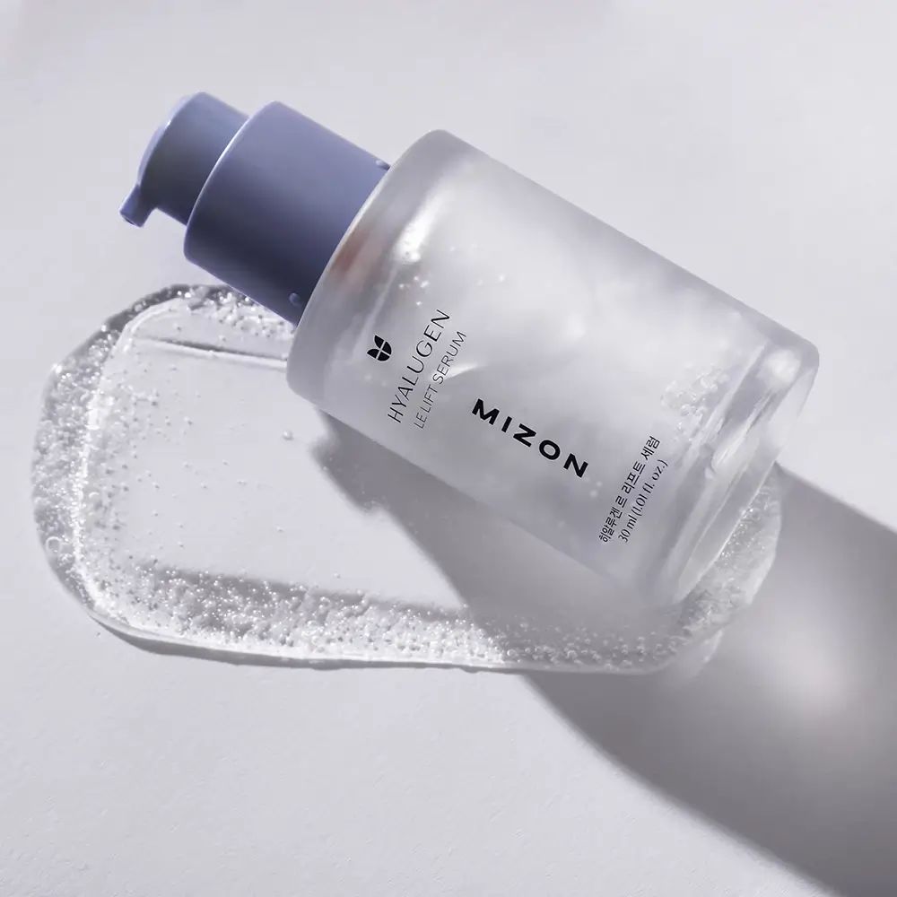 Serumfles ligt op een serumspoor. Opschrift: HYALUGEN LE LIFT SERUM, MIZON. Serumspoor met bellen.