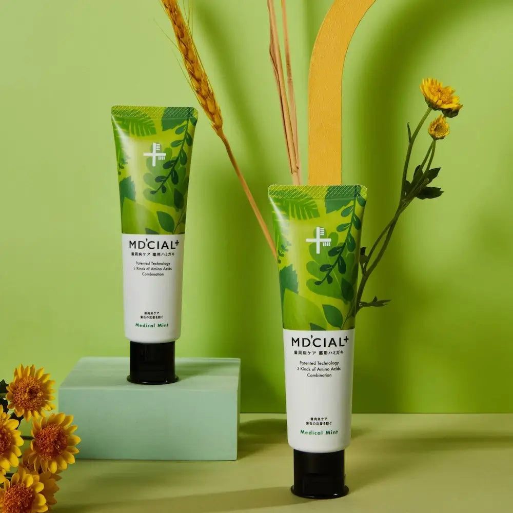 Deux tubes de dentifrice MD'CIAL+. Design vert, inscription Medical Mint. Bouchon noir. Décoration florale.