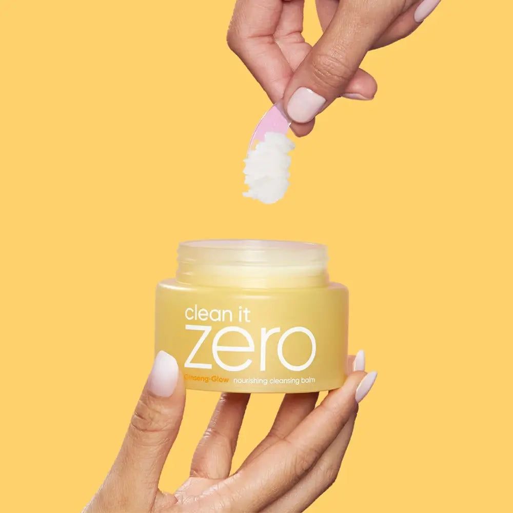 Pot jaune avec inscription "clean it zero", une main soulève une spatule avec du baume blanc.