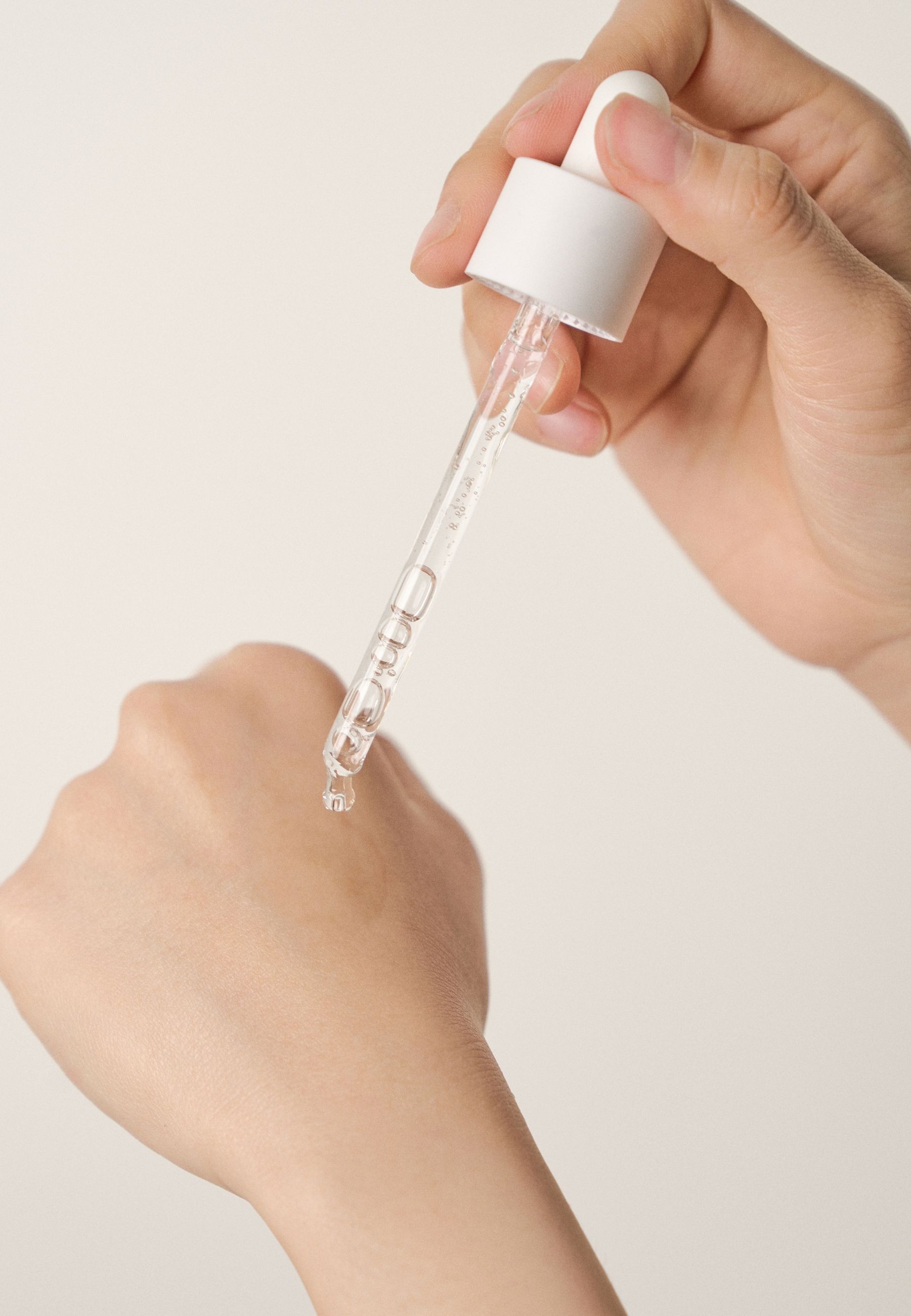 Main tenant une pipette avec du sérum. Goutte de sérum sur la main. Peau claire. Fond clair.