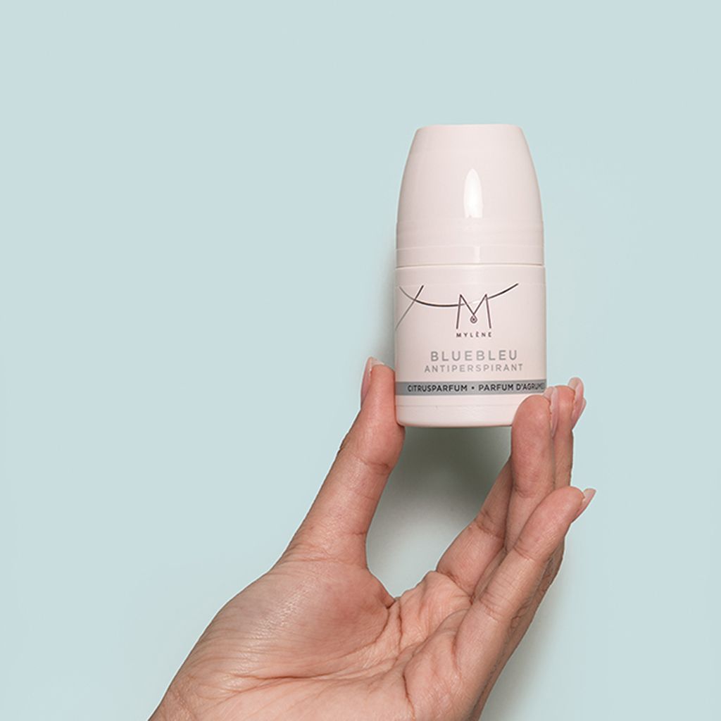 Hand die een witte roll-on deodorantfles vasthoudt met blauw etiket en opschrift "Mylène Bluebleu Antiperspirant".