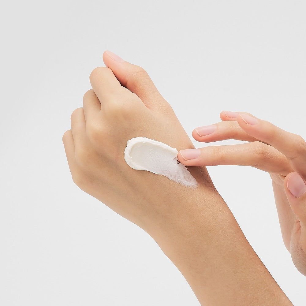 Een hand brengt witte crème aan op de onderarm.
