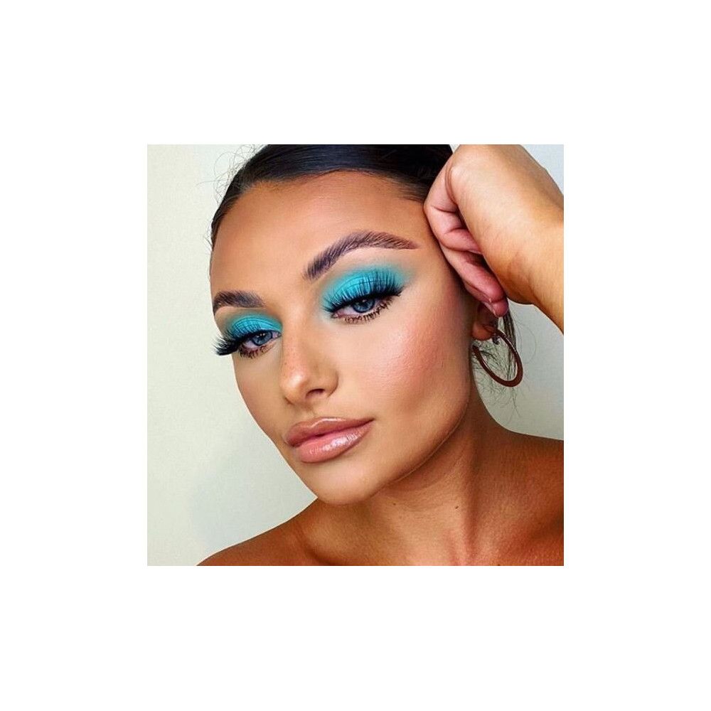 Gros plan d'une femme avec des yeux bleus maquillés et de faux cils. Elle touche ses cheveux.