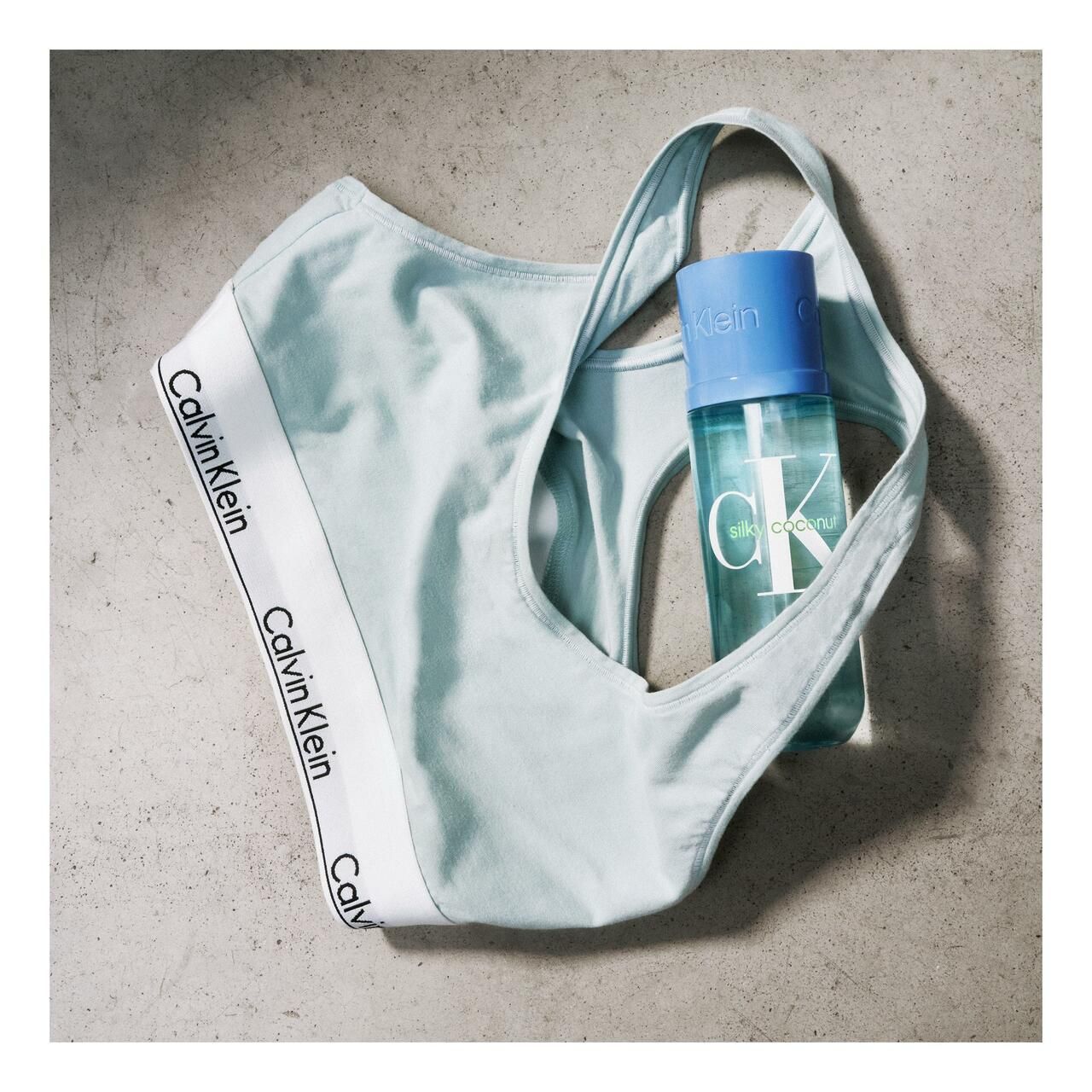 Soutien-gorge de sport bleu clair avec logo Calvin Klein blanc. Flacon avec bouchon bleu et logo Calvin Klein à l'intérieur.