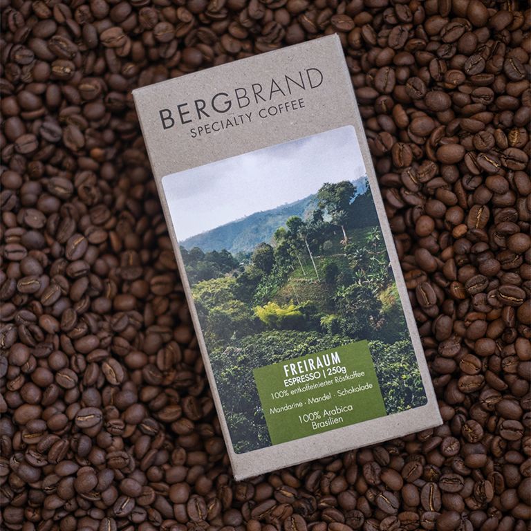 Paquet de café avec paysage. Texte : BERGBRAND, Freiraum Espresso, 100% Arabica, Brésil, Décaféiné. Sur grains.