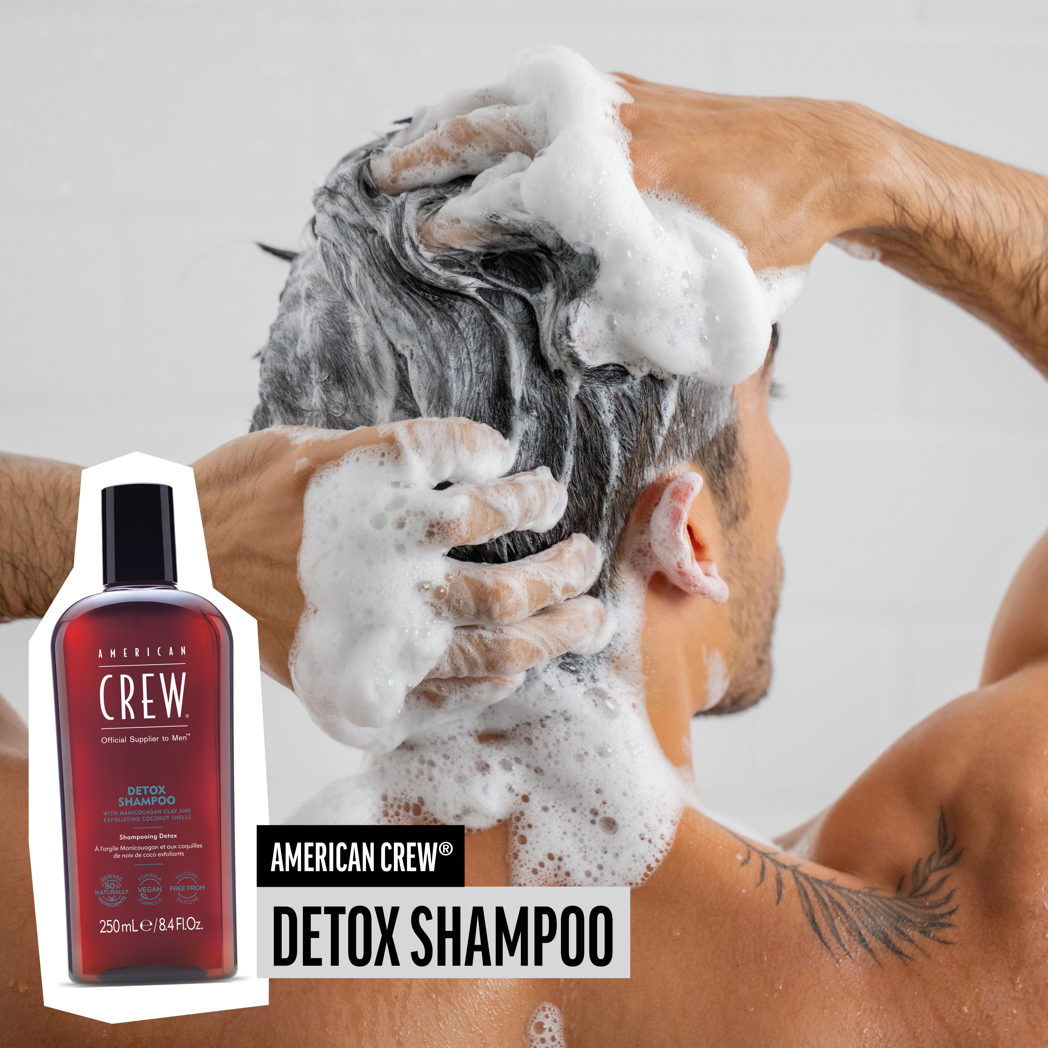 Man wast zijn haar met schuim. AMERICAN CREW Detox Shampoo fles ernaast.