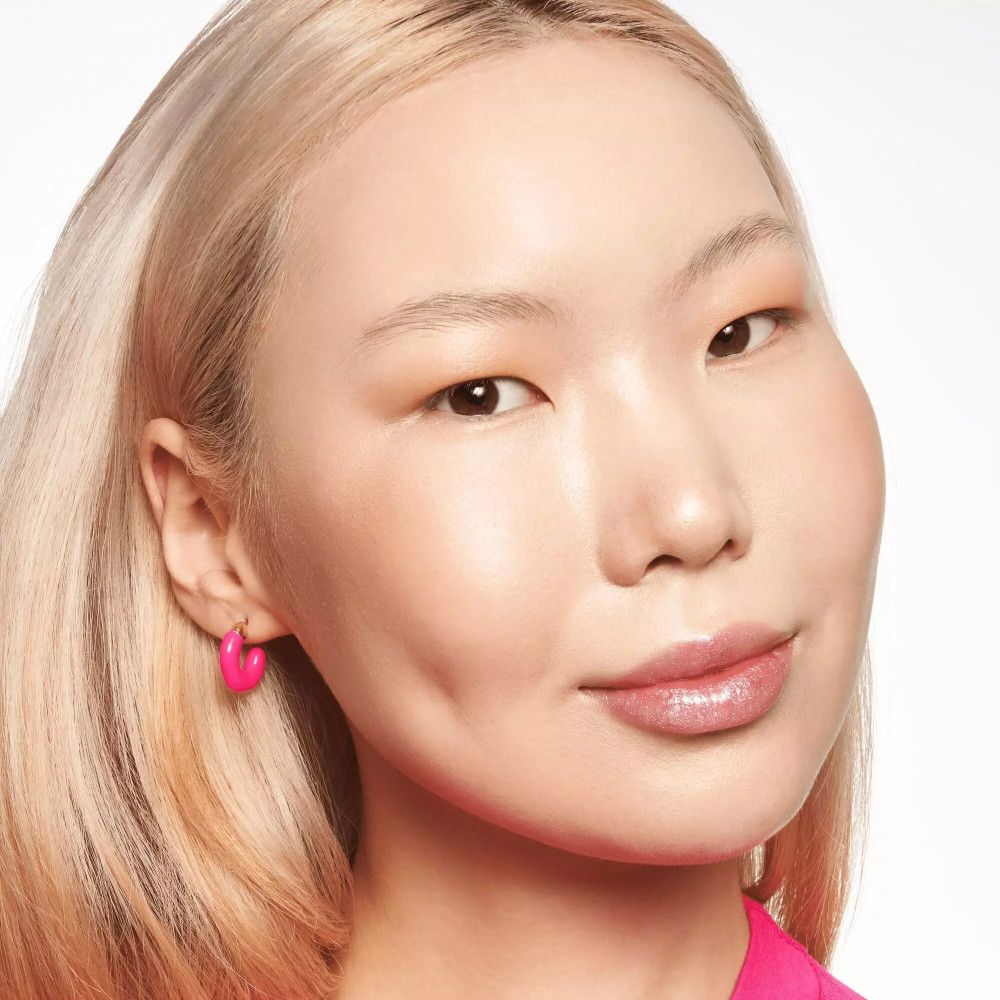 Gros plan d'une femme maquillée. Elle porte des boucles d'oreilles roses et du rouge à lèvres. Teint clair.