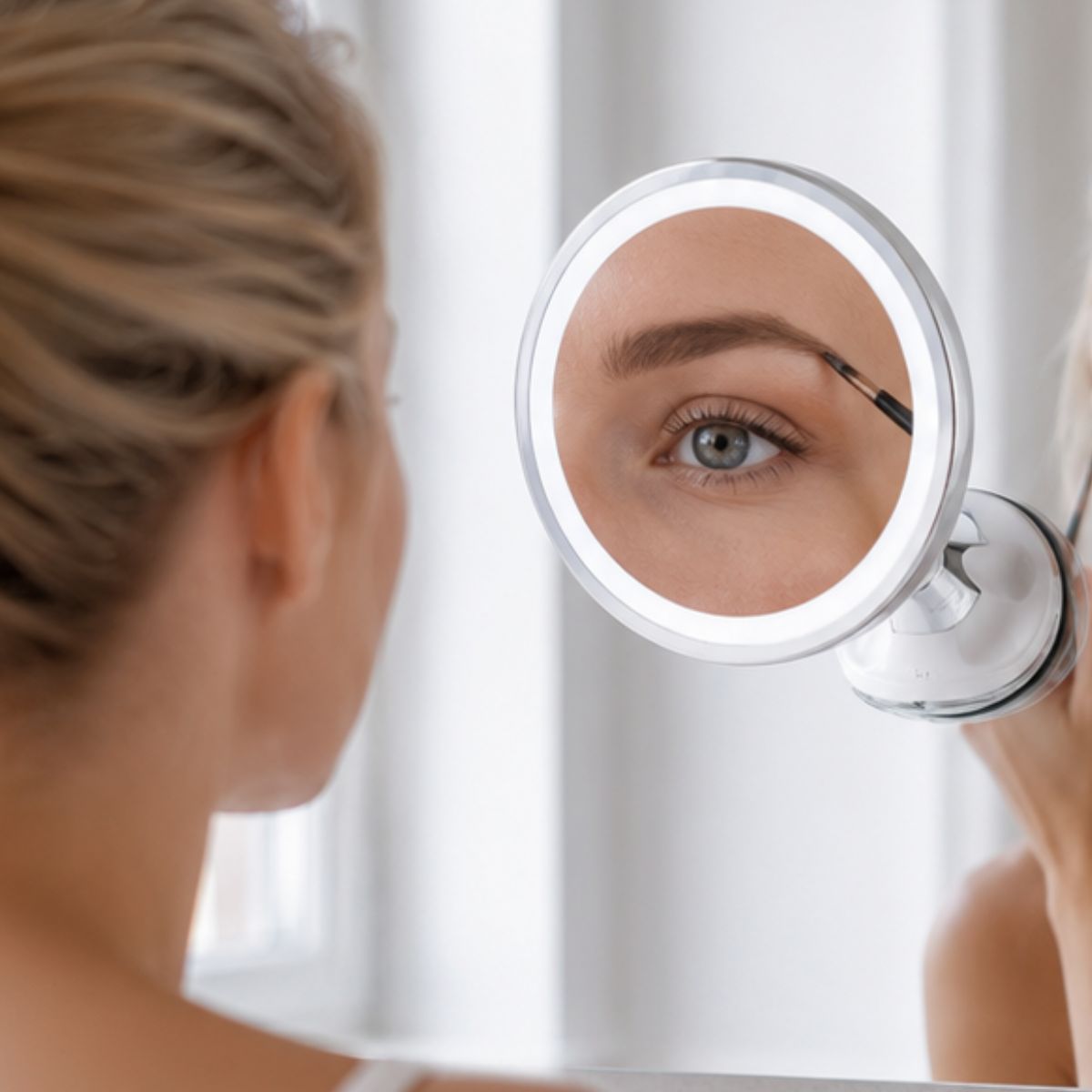 Une femme utilise un miroir rond à LED pour la mise en forme des sourcils.