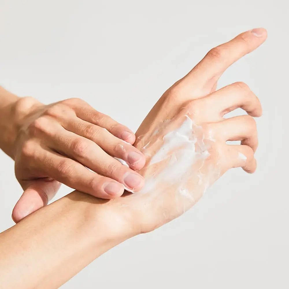 Mains, une frottée de crème. La crème est blanche. Peau claire. Le fond est clair.