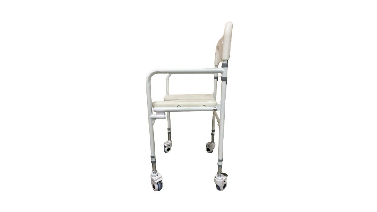 Chaise de douche pliable à roulettes. Vue latérale. Siège et dossier beiges, cadre blanc, accoudoirs. Quatre roues.