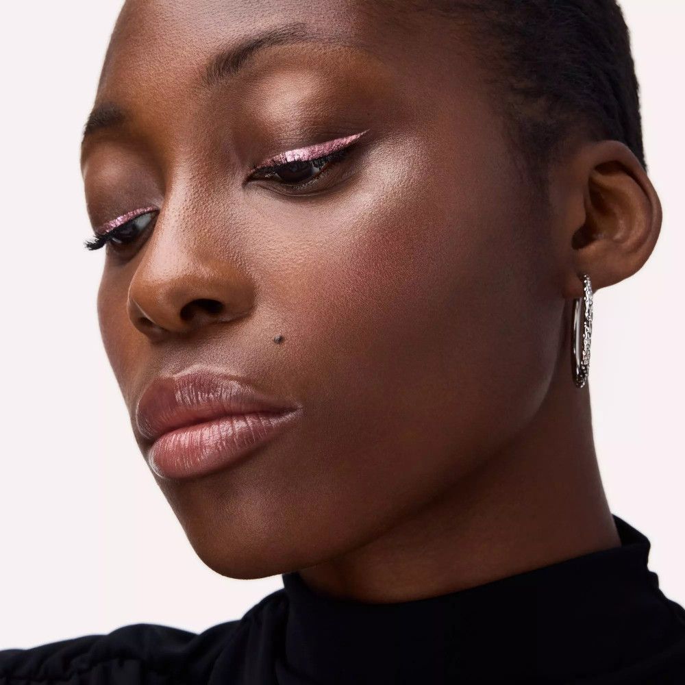 Gros plan d'une personne avec un eyeliner rose. La personne porte des boucles d'oreilles et un haut noir.