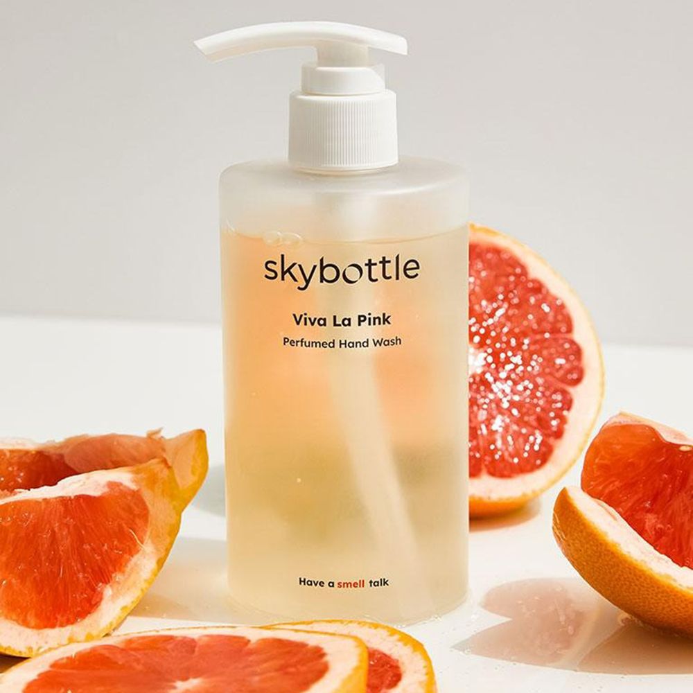 Vloeibare zeep met dispenser en stukjes grapefruit. Opschrift: skybottle, Viva La Pink, Perfumed Hand Wash. Gelige vloeistof.