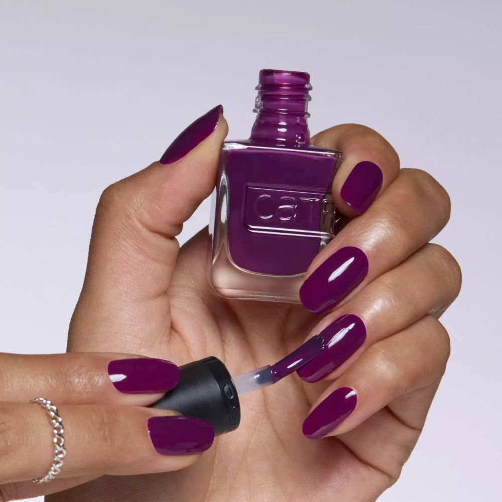 Main avec ongles vernis. Vernis à ongles violet foncé. Flacon avec pinceau. Sur fond clair.