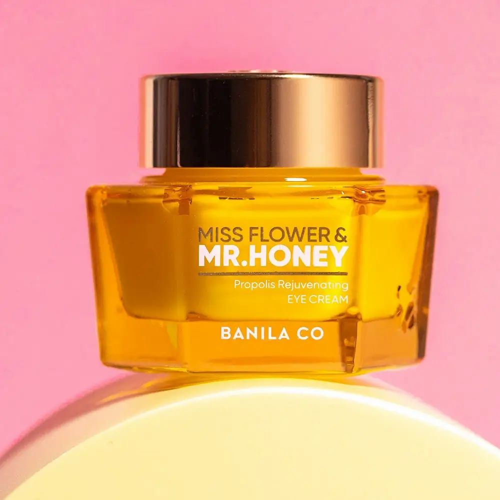 Gouden oogcrème potje. Opschrift: Miss Flower & Mr. Honey, Propolis Rejuvenating Eye Cream, BANILA CO. Op roze achtergrond.
