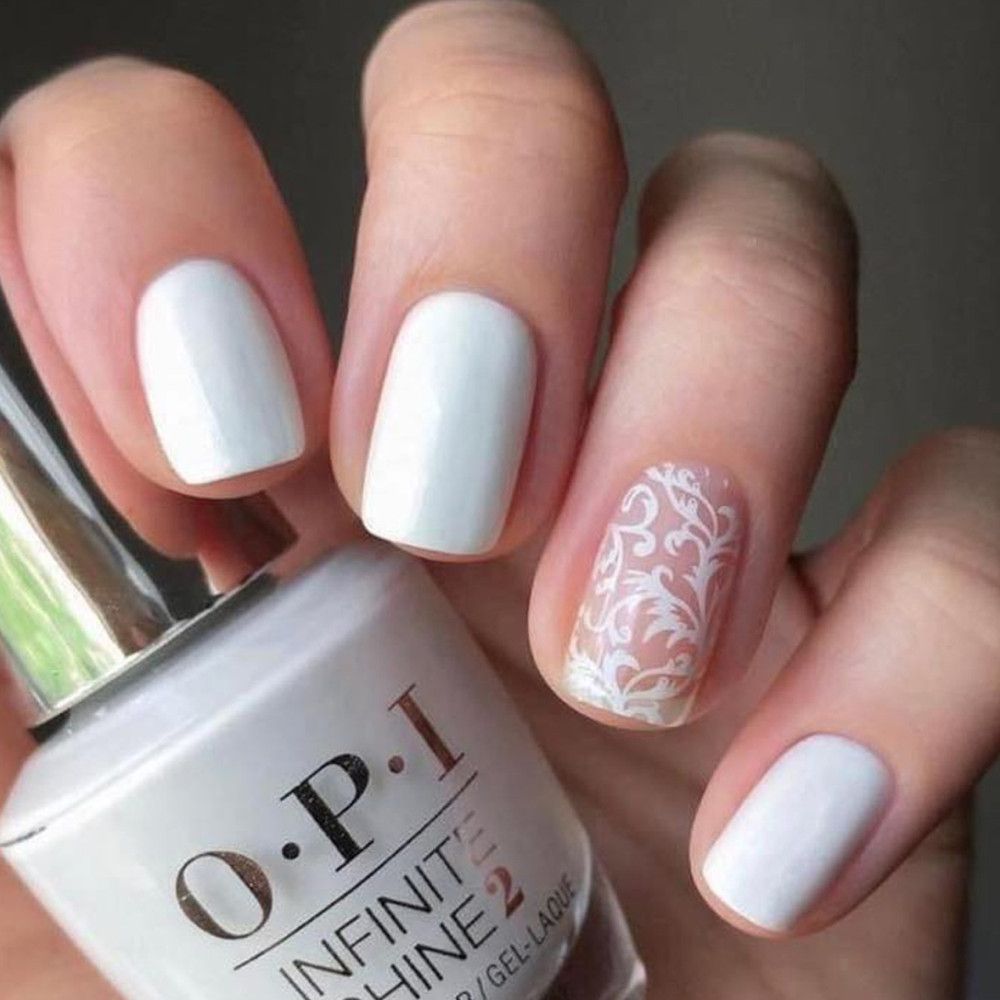 Mains avec ongles vernis blancs et flacon de vernis à ongles. Un ongle avec motif de dentelle blanche. OPI Infinite Shine 2.