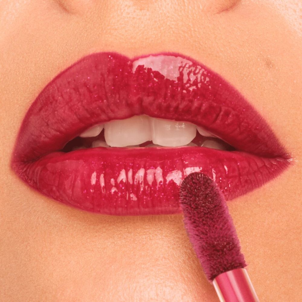Close-up van lippen met rode lipgloss. Een applicator wordt gebruikt. De lippen glanzen.