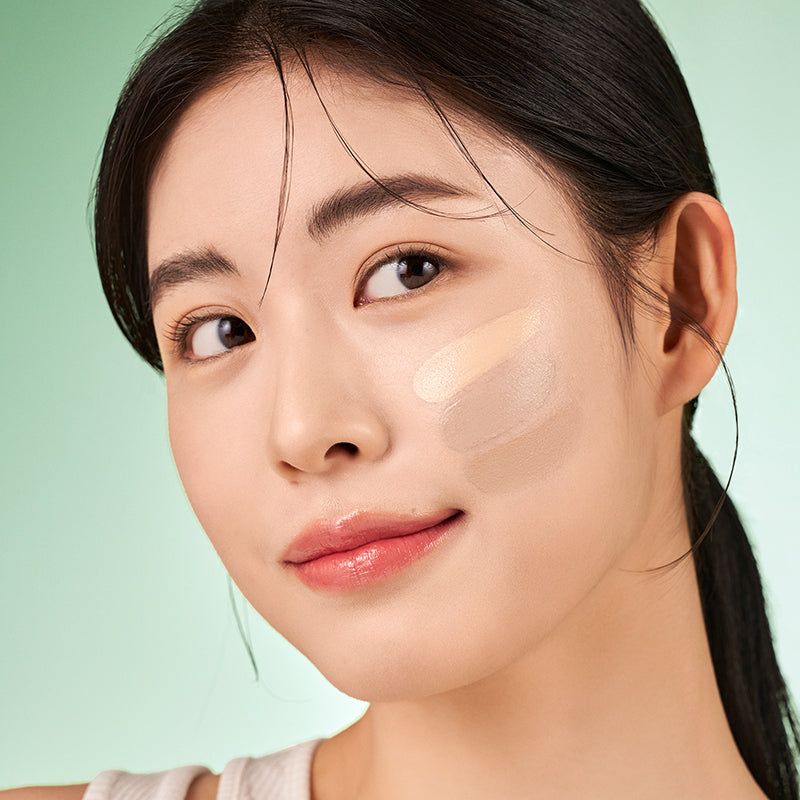 Vrouw met getinte crème op de wang. Twee tinten zichtbaar. Groene achtergrond.