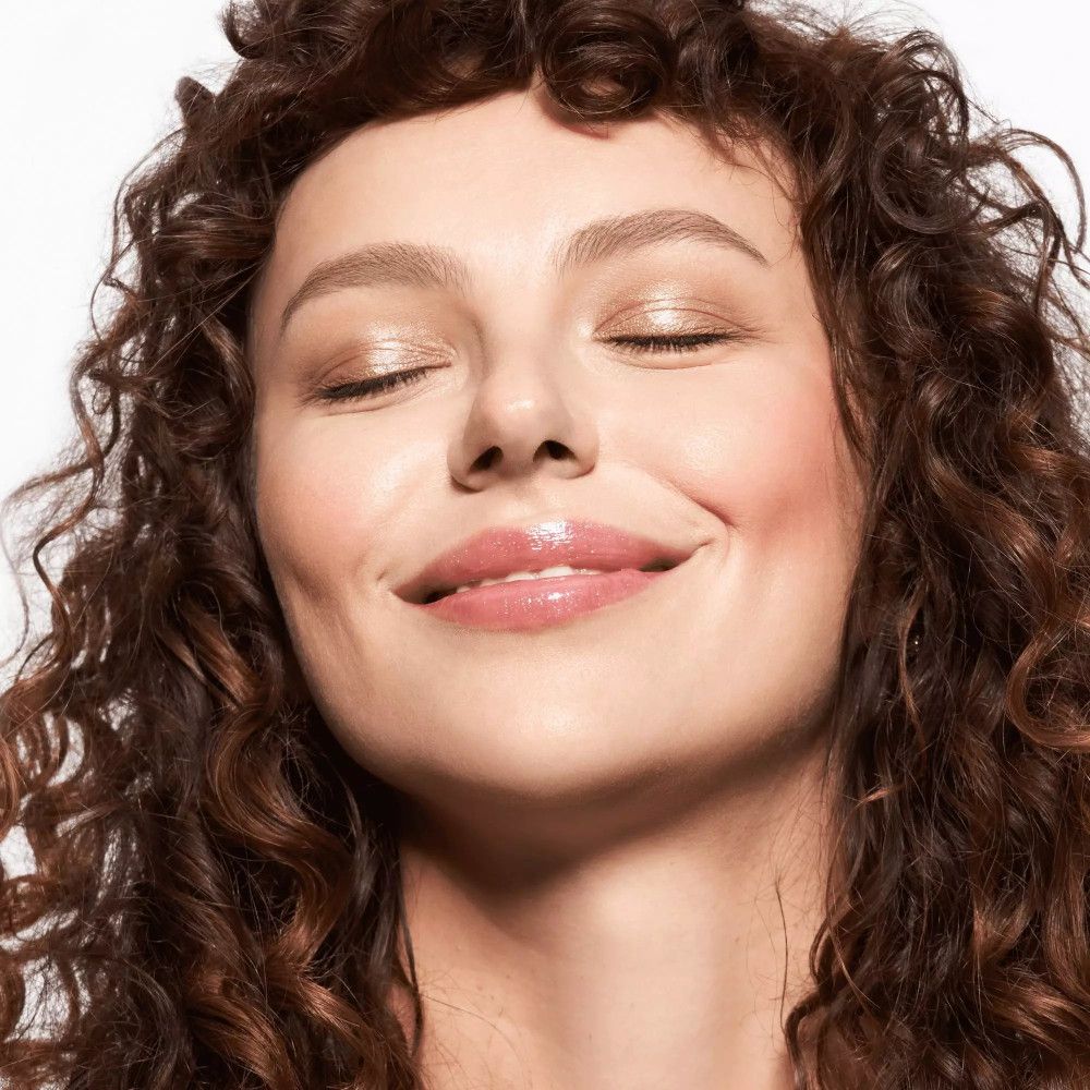 Femme aux yeux fermés, lèvres brillantes. Teint clair. Cheveux bouclés.