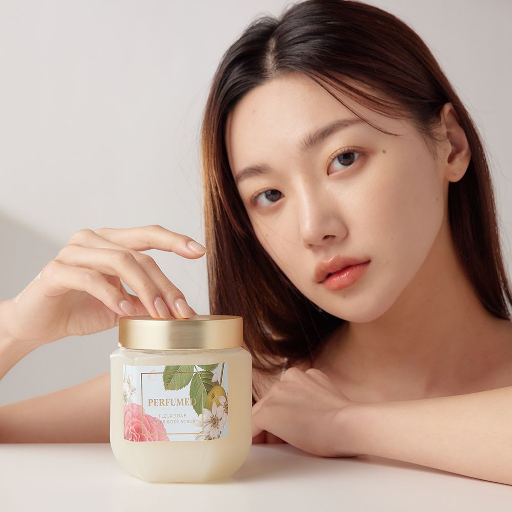 Femme tenant un pot en verre avec couvercle doré. Étiquette avec motif floral et inscription PERFUMED.